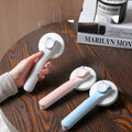 Three window cleaning squeegees in white, pink, and blue on a wooden surface with a hand holding one.